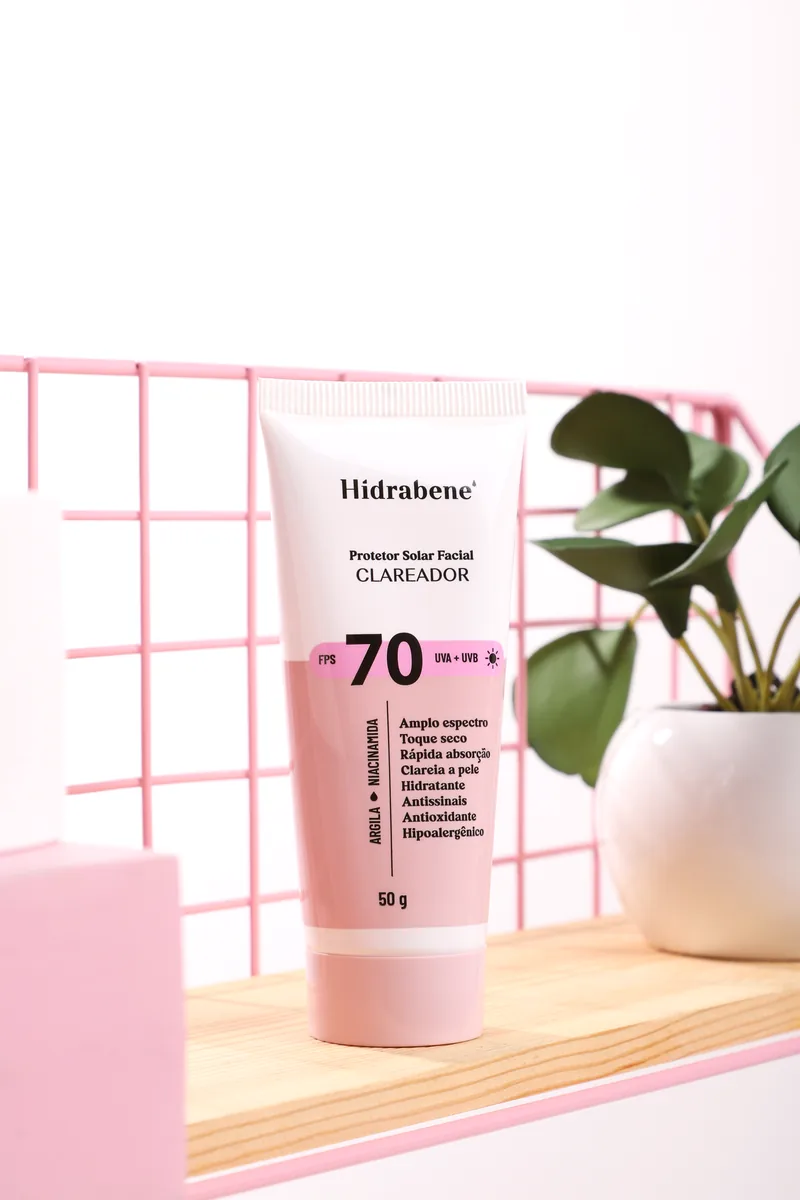 Bisnaga do Protetor Solar Facial FPS 70 Clareador Hidrabene em cenário com grade rosa e planta